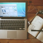 Image of a Macbook open on a desk close to a pencil and notebook